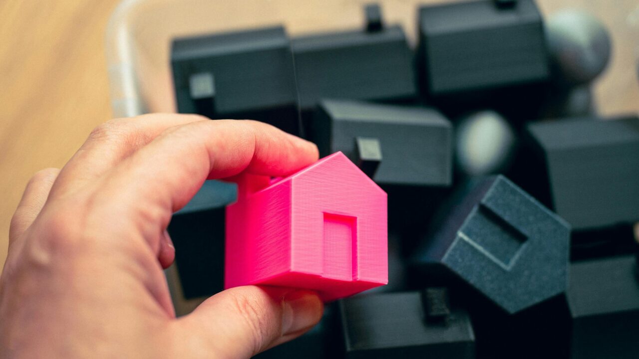 Hand holding a pink house model among black ones, symbolizing equity access options with Yellow Brick Road Home Loans.